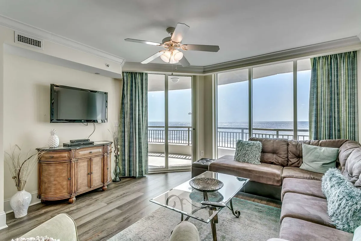 A spacious open-concept living area with a plush sectional sofa, decorative coffee table, and a TV unit. The scene is bathed in natural light pouring through large windows that offer stunning ocean views, perfectly capturing the cozy yet elegant coastal décor highlighted in the section. The arrangement invites guests to relax, socialize, or enjoy entertainment while always remaining visually connected to the ocean beyond.