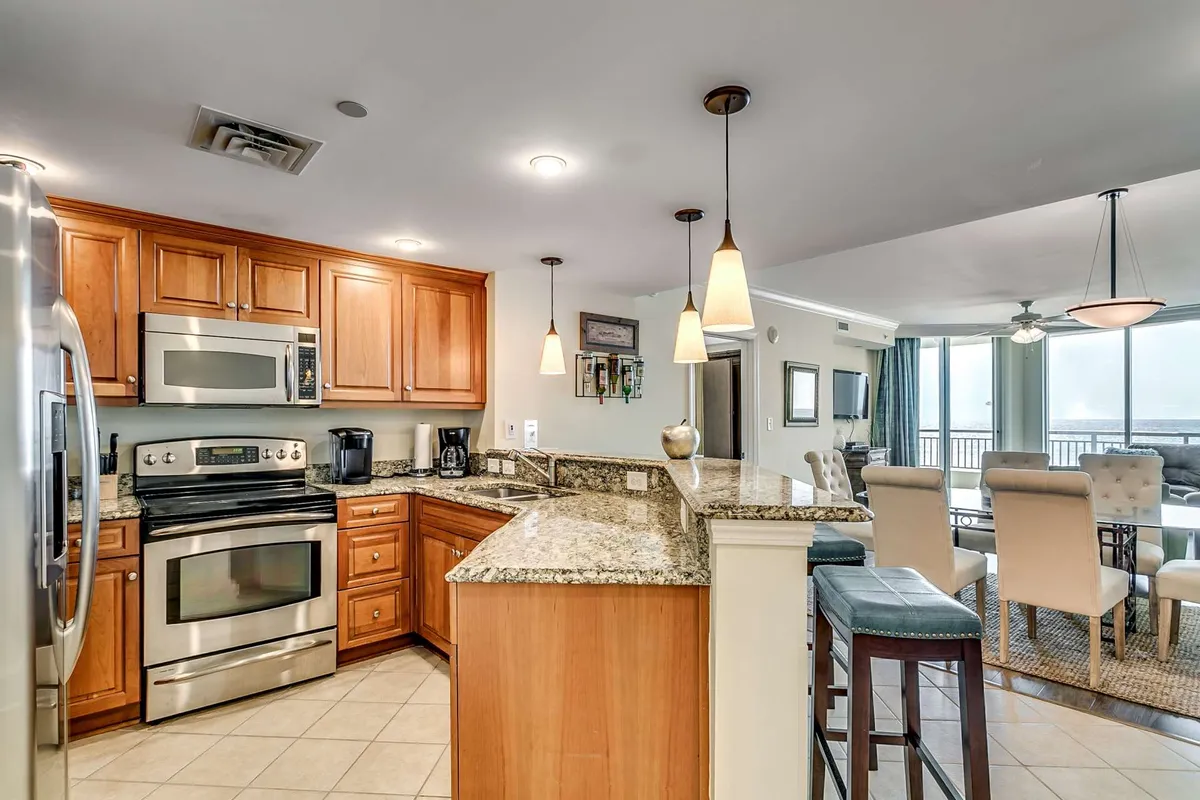 A warm dining area adjacent to the kitchen, featuring a granite countertop, stainless steel appliances, wood cabinetry, and a view into the dining space. The area is well-lit and welcoming, designed for both casual family meals and more formal entertaining, capturing the sense of togetherness described in the section.