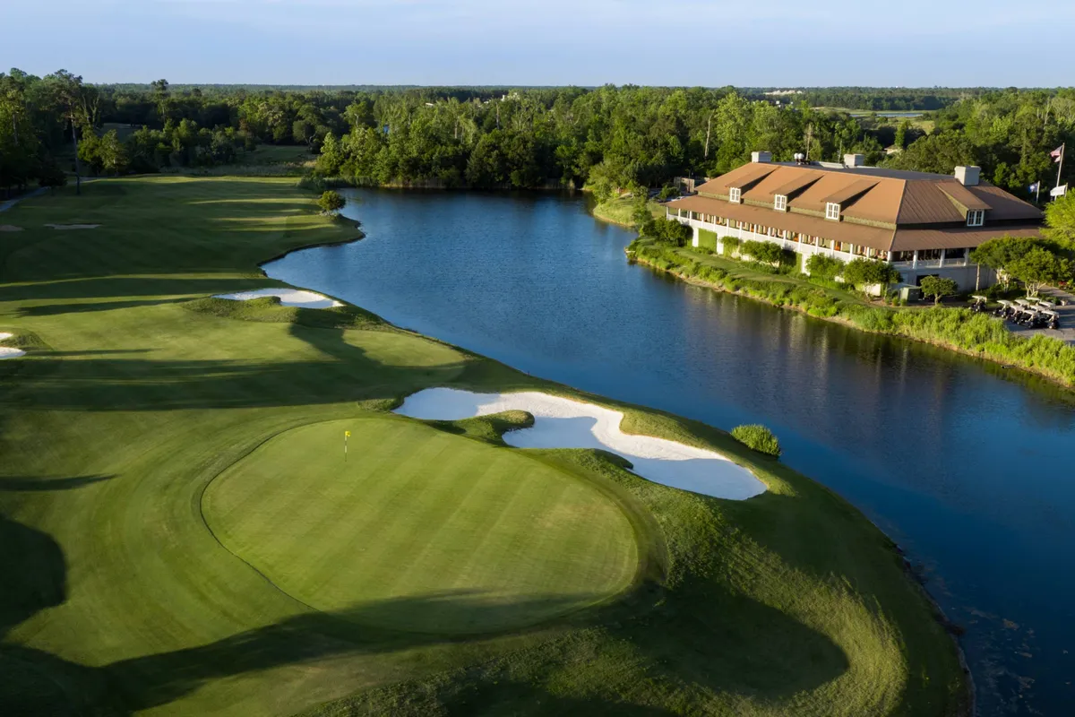 A scenic golf course with rolling greens, a serene water body, a clubhouse in the background, and sand traps visible. The setting sun adds a warm glow to the landscape, capturing the leisurely, exclusive experience of golfing.