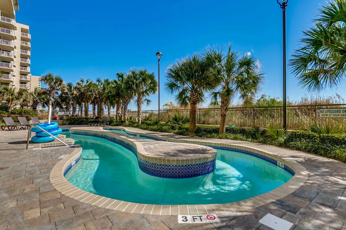 A sparkling swimming pool is surrounded by palm trees and inviting lounge chairs. The tranquil setting suggests both family fun and relaxation, with ample space for guests of all ages to enjoy the outdoors together.
