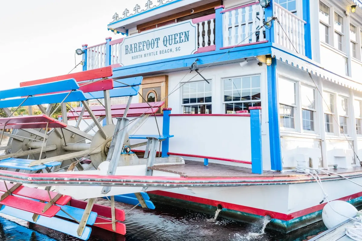 The colorful exterior of the Barefoot Queen paddlewheel cruise boat, complete with its iconic paddle wheel and signage. The image radiates a playful and festive atmosphere, hinting at the unique local adventures available to guests, such as riverboat cruises and evening events on the water.