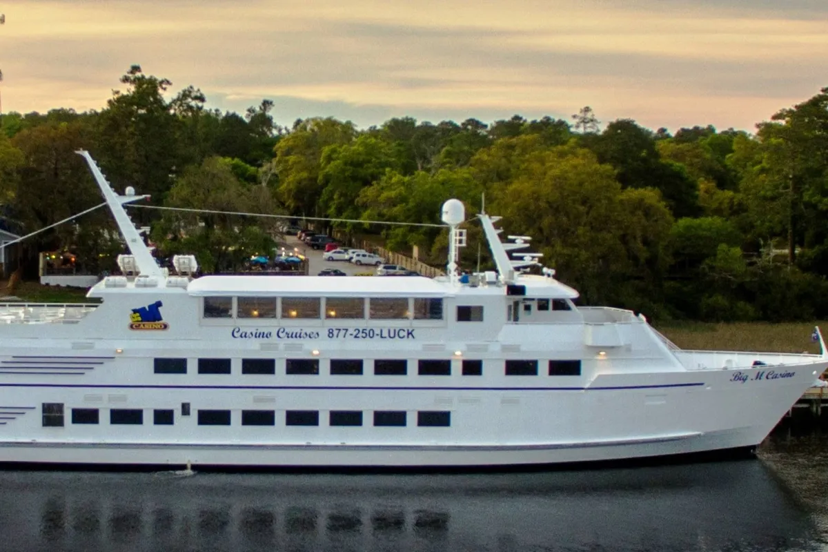 A large cruise ship glides along the river, surrounded by lush trees and reflecting water. The scene hints at onboard social activities—dining, entertainment, and gambling—with a sunset atmosphere that’s both relaxing and energizing for group outings.